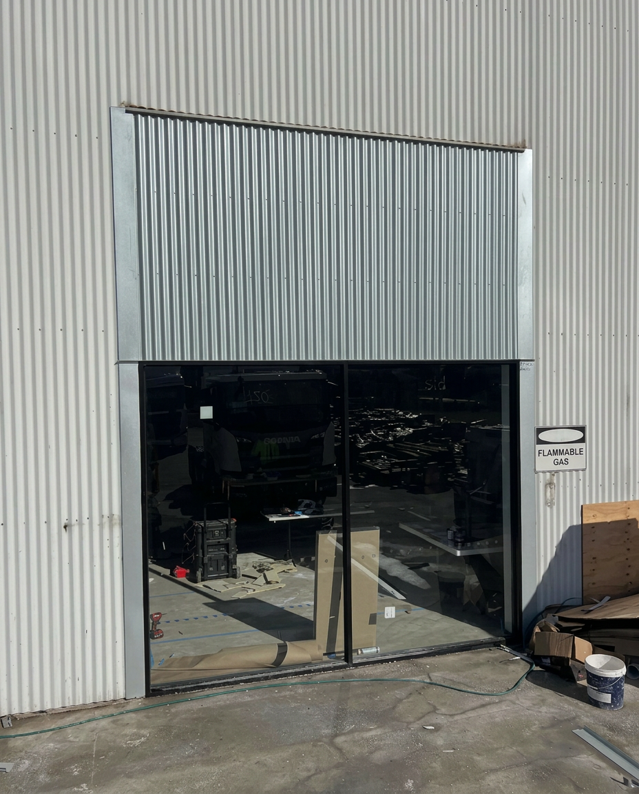 Corrugated metal wall cladding and edge flashings around glazed industrial doors